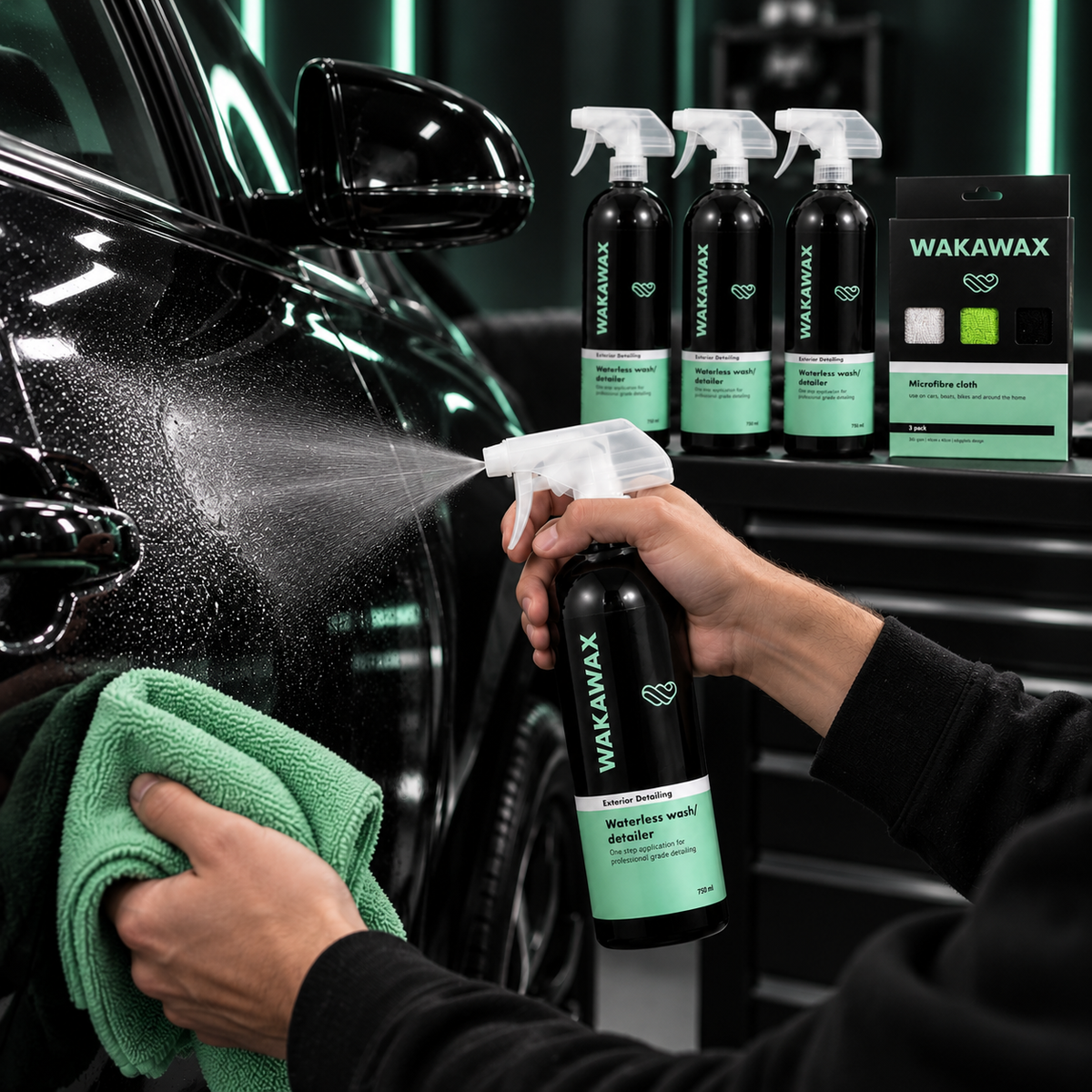 Spraying WakaWax waterless car wash onto a black car door and wiping it with a green microfibre cloth